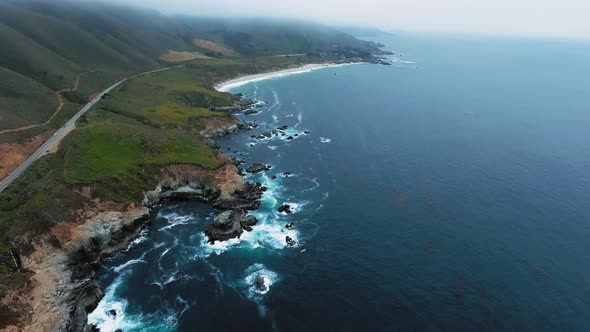 Aerial panoramic footage of road and green rocky ocean shore in Big Sur, California, USA alt