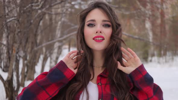 Young Woman with Wavy Hair Standing and Touching Face in Winter Forest