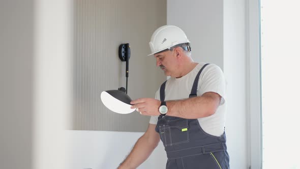 An Elderly Electrician Checks the Operation of the Wall Sconces of the Lamp in the House After alt