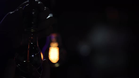 A man twists in a decorative light bulb and it lights up in the dark copy space.