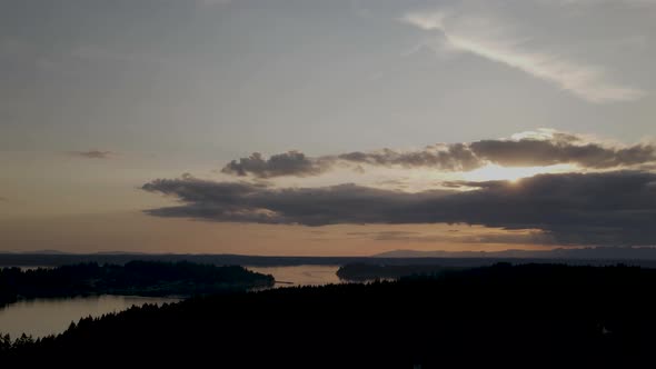 Dark clouds spread across a golden hazy sunset over Puget Sound, Washington, aerial hyperlapse alt