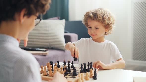 Emotional Young Kid Playing Chess with Mommy Moving Pieces on Board and Smiling alt