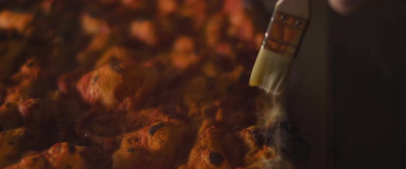 Chef spreading olive oil over freshly baked pizza dough with tomato sauce. Close up, slow motion. alt