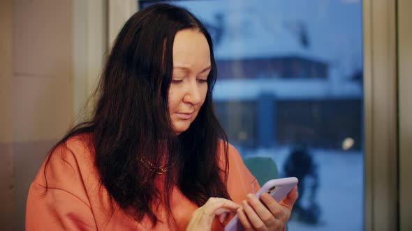 Brunette Woman Texting Message in Mobile Phone on Window Background alt
