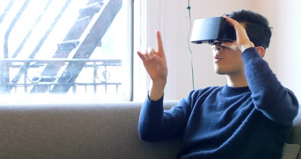 Man gesturing while using virtual reality headset in living room 4k alt