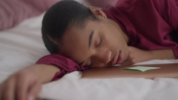 Closeup Portrait of Young Exhausted African American Woman Sleeping Lying on Bed with Laptop alt