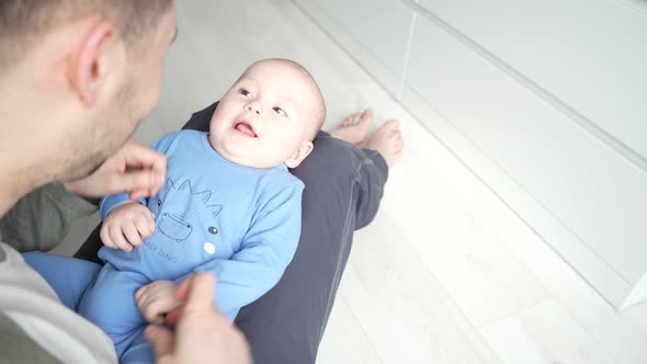 Father Plays with a Smiling Baby Son Lying on Knees at Home Together