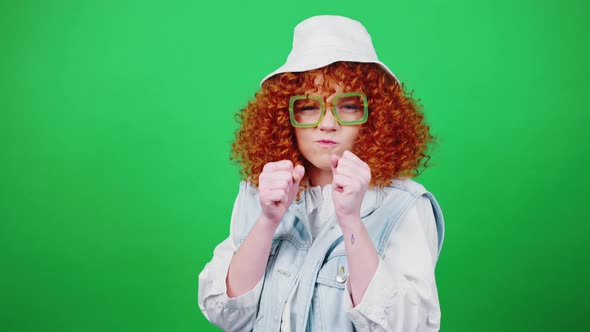 Playful Redhead Curly Lady in Glasses and Panama Hat Joking Boxing to Camera and Laughing Green alt