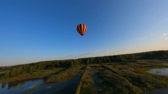 Drone flying close to black and orange hot air balloon floating above lake