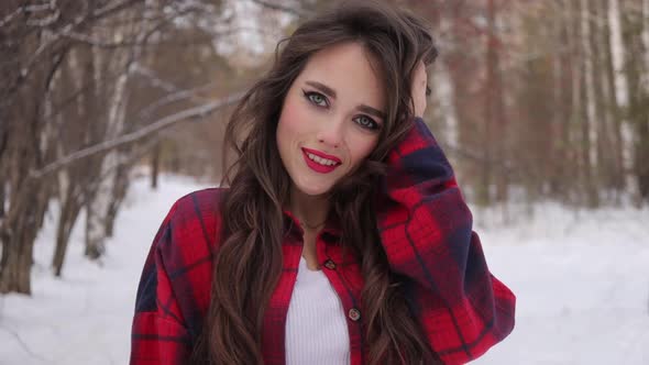 Young Woman with Wavy Hair Standing and Touching Face in Winter Forest