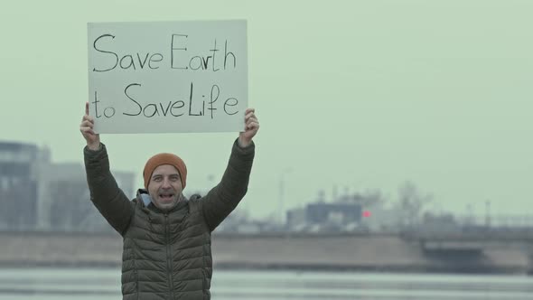 Eco Activist Standing with Poster on Polluted Seashore alt
