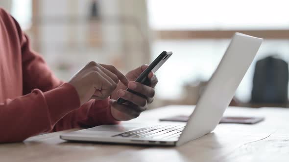 Hands Close up of African Man with Laptop using Smartphone alt