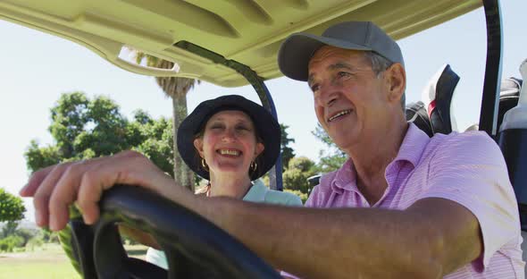 Caucasian senior couple driving a golf cart with clubs on the back at golf course alt