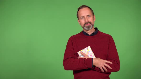 A Middleaged Handsome Caucasian Man Holds a Book and Smiles at the Camera  Green Screen Background