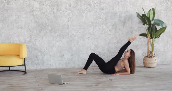 Full Length of Young Woman Training at Home in Front of Laptop Lying on Floor Near Home Plant and alt