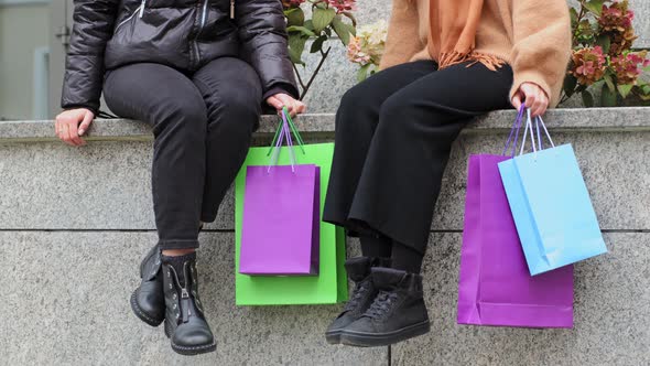 Two Unrecognizable Women Shoppers Sitting on Street in City Girlfriends After Shopping Discounts on alt