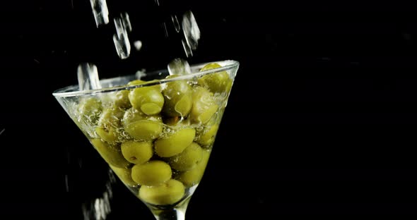 Cocktail being poured into the glass full of olives alt