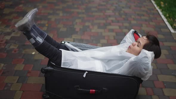 Joyful Carefree Little Woman Lying in Travel Bag Shaking Legs Smiling alt