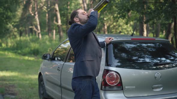Side View Portrait of Young Drunk Caucasian Businessman in Suit Standing at Car on Suburban Road alt