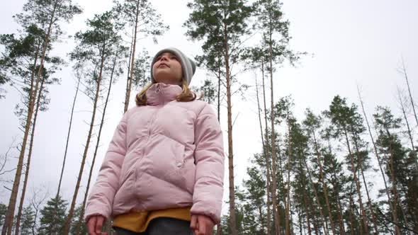 The Child Spins and Looks at the Tops of Pine Trees in the Park alt