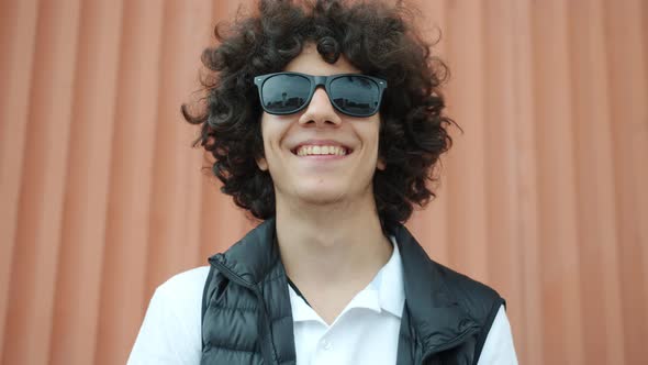 Portrait of Handsome Middle Eastern Teenage Boy Standing Outdoors Wearing Sun Glasses Smiling alt