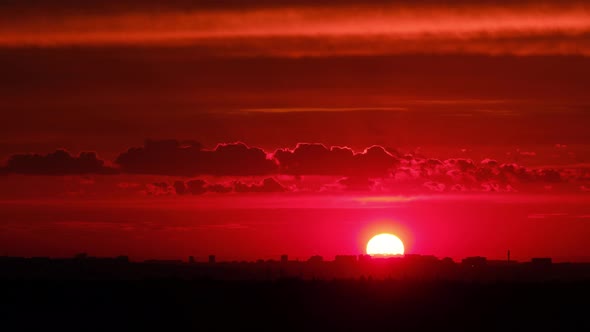 The silhouette of the night city in the light of the setting red sun alt
