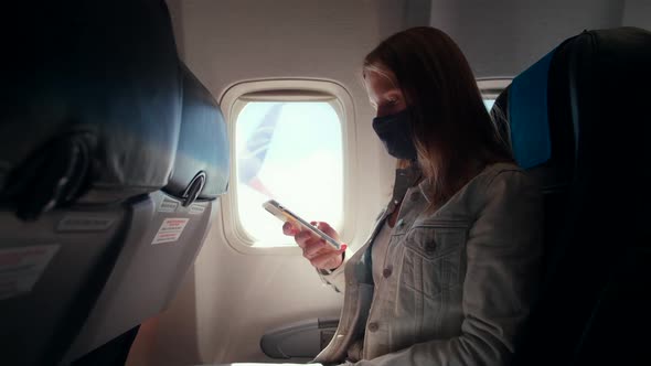 Woman in Mask Uses Phone During Flight in Airplane. Safe Traveling at COVID-19