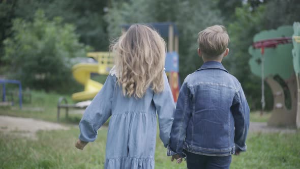 Back View of Little Caucasian Boy and Girl Holding Hands and Walking To Playground alt