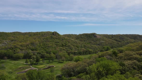 Aerial view of valley with golf course running through the base. Mountains covered in trees.