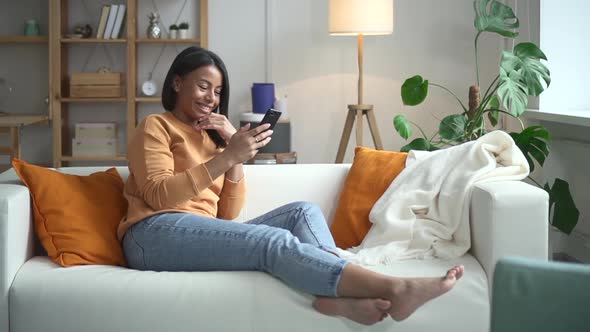 Woman Using Phone and Smiling Sitting on Couch in Light Room Spbd alt