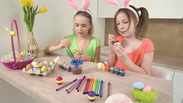 Girls with Rabbit Ears on Their Heads Decorate Easter Eggs with Paint