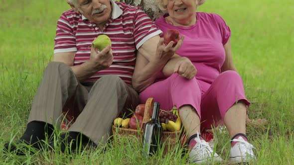 Family Weekend Picnic in Park. Active Senior Old Caucasian Couple Sit on Blanket and Eating Fruits alt