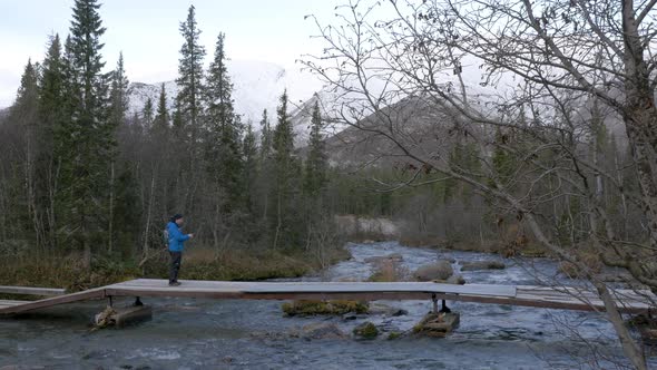A Man Traveler Crosses a Mountain Stream Over a Bridge. Beautiful View alt