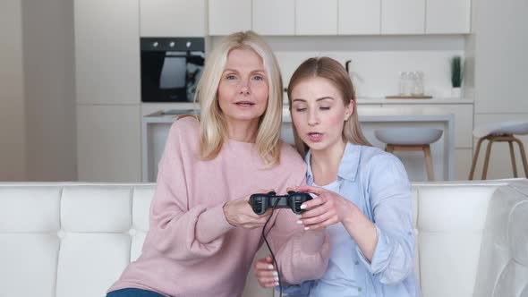 Happy Grown Daughter Teach Her Senior Mother to Play Video Games on Console While Sitting on Couch alt