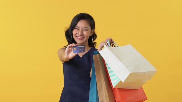 Pretty smiling young Asian woman holding shopping bags and showing credit card