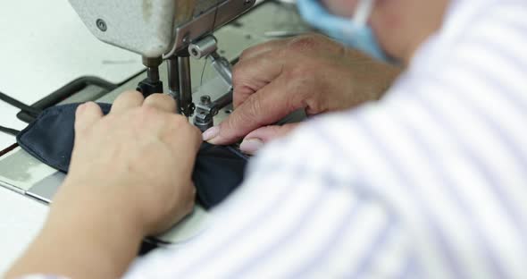 A Sew Factory Seamstress Stitching Vertically The Folded Edges Of The Blue Face Mask - Covid-19 Pand alt