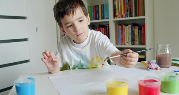 Boy Reaching for Paints With Paintbrush and Painting