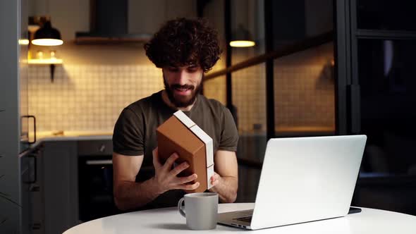 Happy Surprised Beared Young Man Opening Gift Box with Present During Video Call on Laptop Computer alt