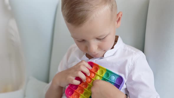 Portrait blonde boy with pop it sensory toy different forms. alt