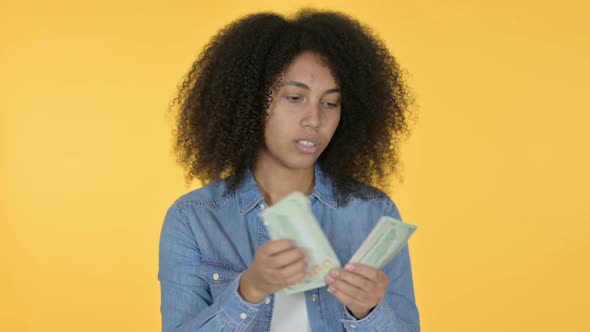 African Woman Counting Dollars Yellow Background alt