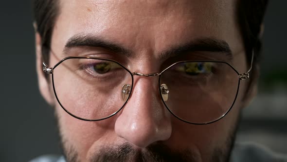 Portrait of serious young man looking at display wearing glasses at home alt