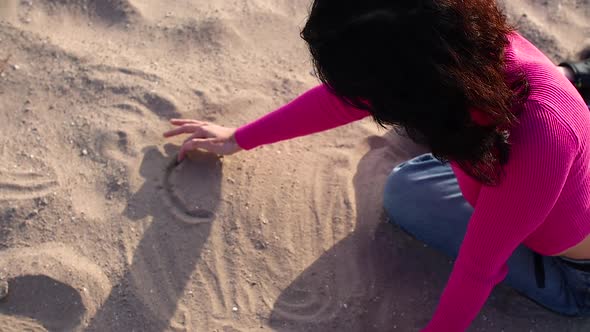 Young Woman Draws a Heart on the Sand Close Up