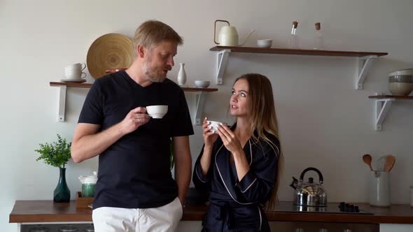 Tall Man and Little Woman Are Drinking Coffee Together at Home Kitchen in Morning at Weekends alt