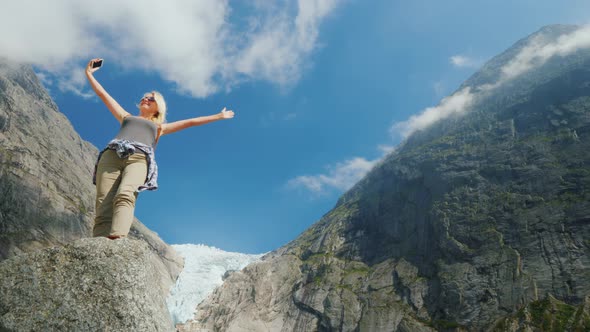 A Successful Young Woman Photographes Herself Against the Backdrop of Mountains and a Glacier in alt
