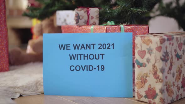 Closeup of Paper with We Want 2021 Without Covid19 Written and Blurred Packed Christmas Gifts at alt