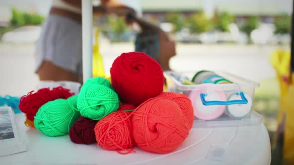 Many Threads and Ribbons Lie on the Table Against the Background of a Girl Whose African Braids are alt