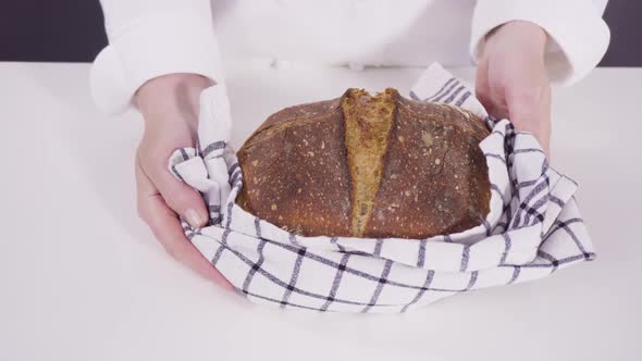 Slicing freshly baked sourdough rye bread on a white cutting board. alt