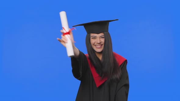 Portrait of Female Student in Cap and Gown Graduation Costume Holding Diploma and Dancing Merrily alt
