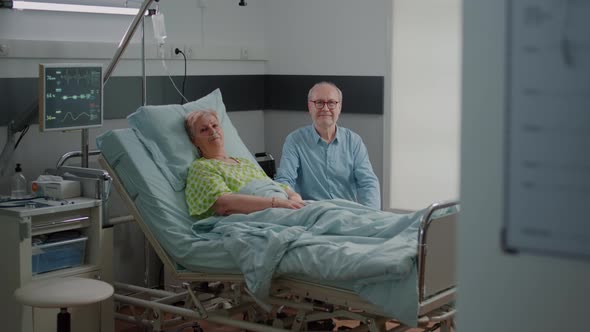 Portrait of Pensioner with Disease Laying in Bed and Man Giving Assistance alt