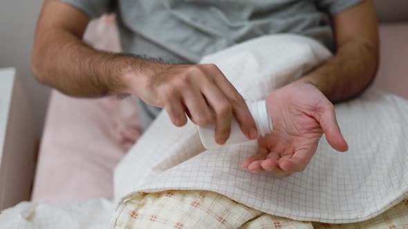 Asian man taking pills into the palm of his hand while in the bedroom at home.